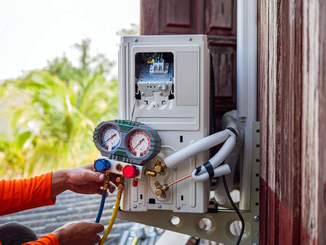 An HVAC technician checking refrigerant pressure levels on an outdoor mini-split heat pump unit using a manifold gauge during a residential heating repair service in Brownsville.