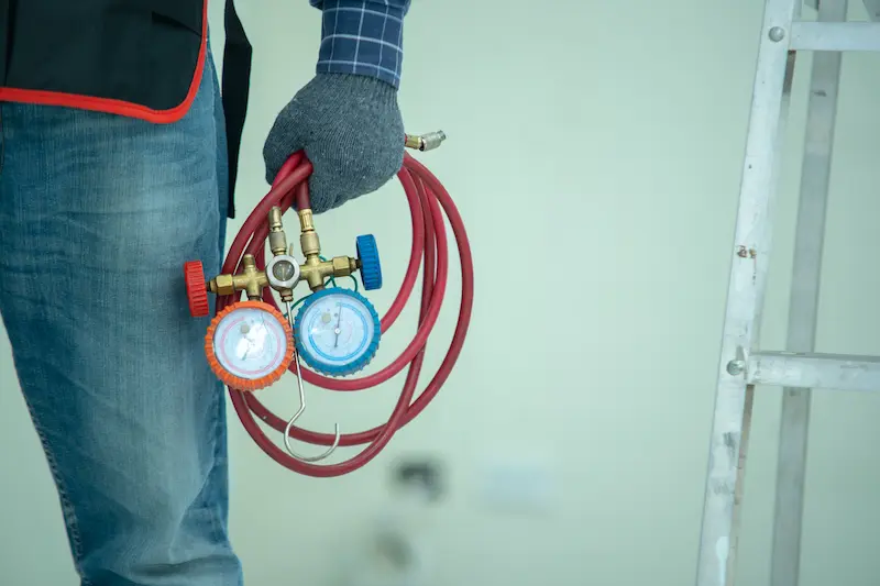 An HVAC technician holding a set of refrigerant manifold gauges for diagnostic testing and service on HVAC in Brownsville.